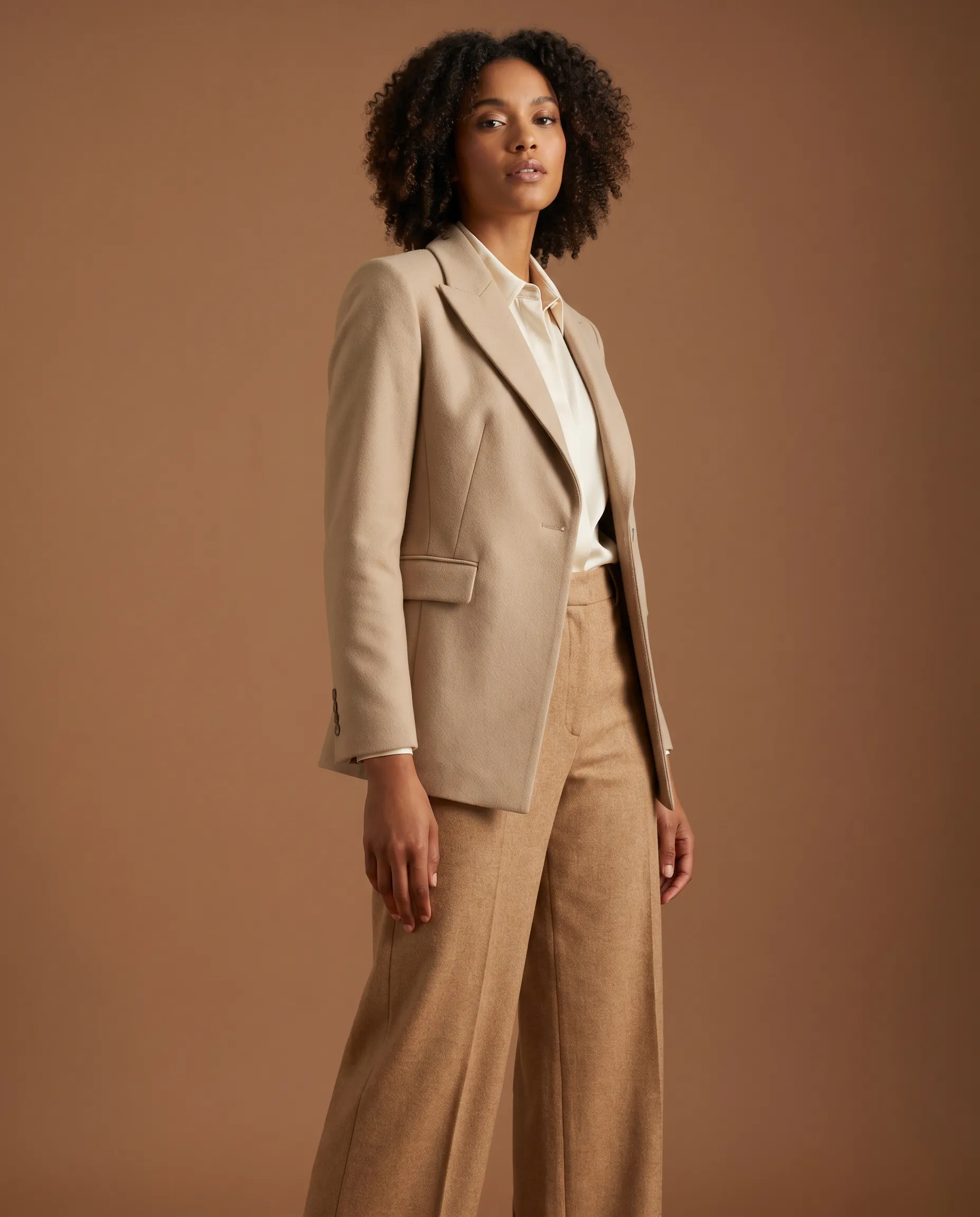 AI-generated on-model fashion photograph: a named AI model wearing a structured garment in a directed three-quarter pose against a clean studio scene, demonstrating pose and scene control